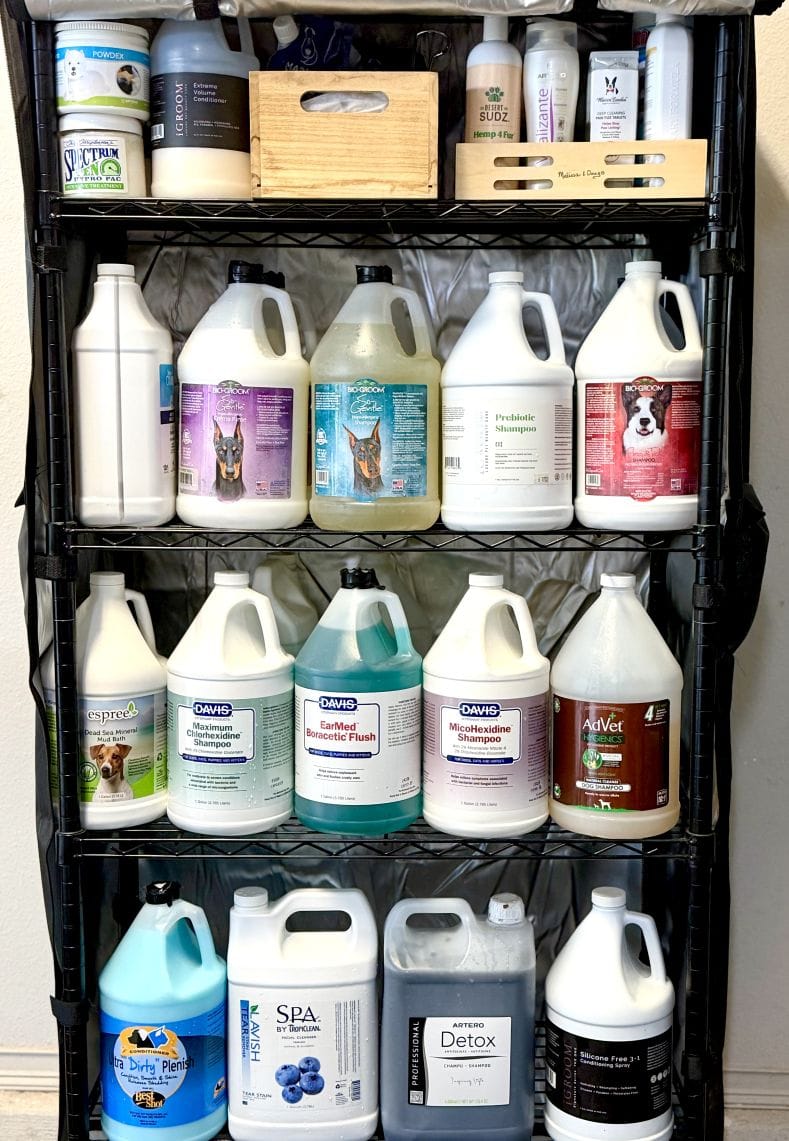 Black wire shelving stacked with gallon bottles of shampoo and conditioner, medicated washes and an ear flush among them.